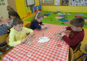 Trójka dzieci skleja z elementów papierowych renifera.